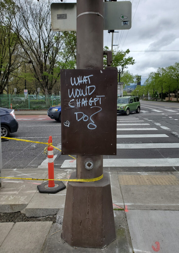 Graffiti "What would ChatGPTDo?" on service box cover attached to street post.